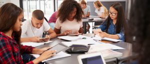 Grupo de estudiantes en iPads sentados en la mesa del aula cuadrada