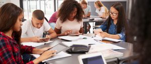 group of students on iPads sitting at square classroom table