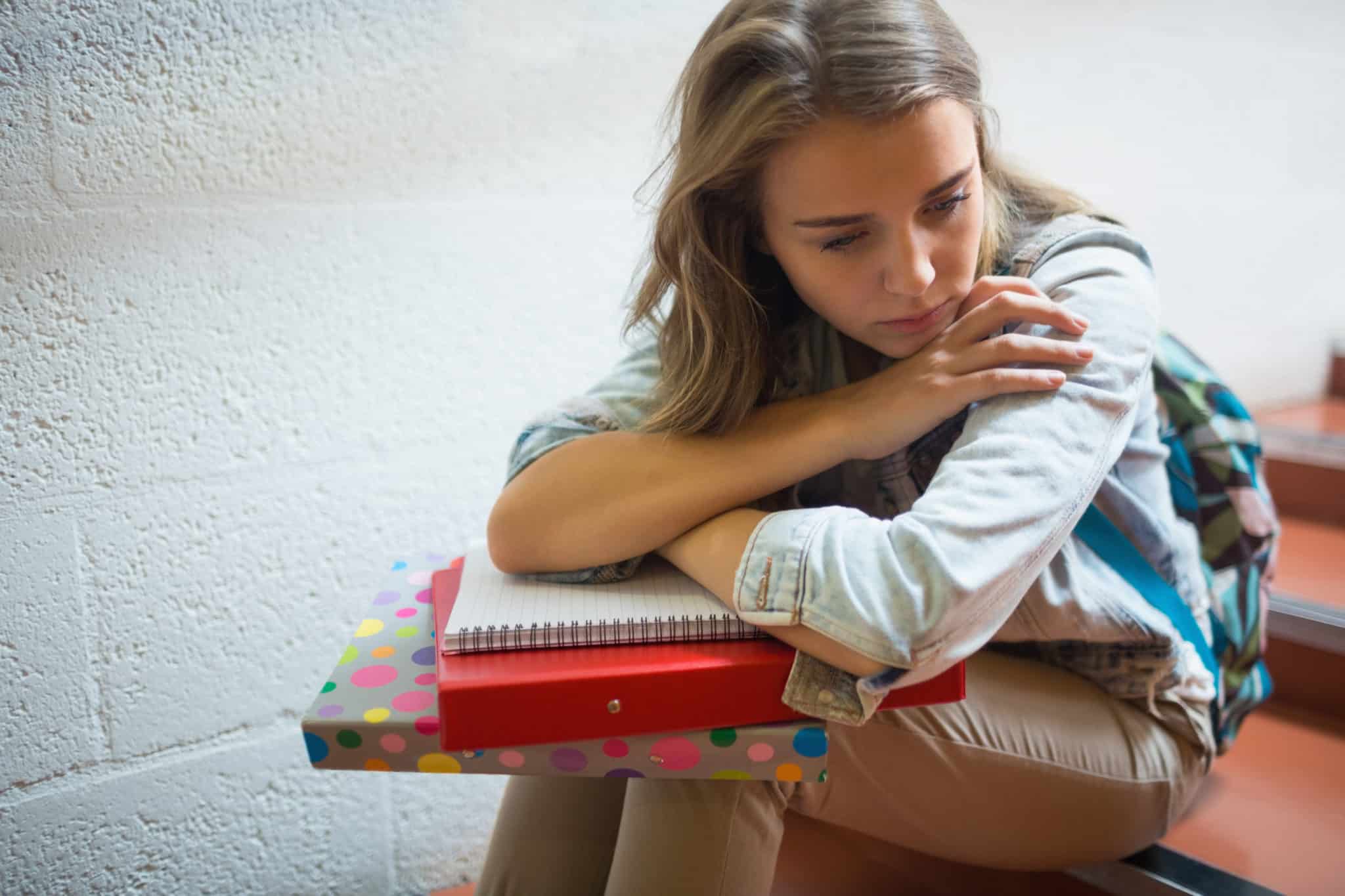 Mädchen mit traurigem Gesicht sitzt auf der Treppe und hat Bücher auf dem Schoß