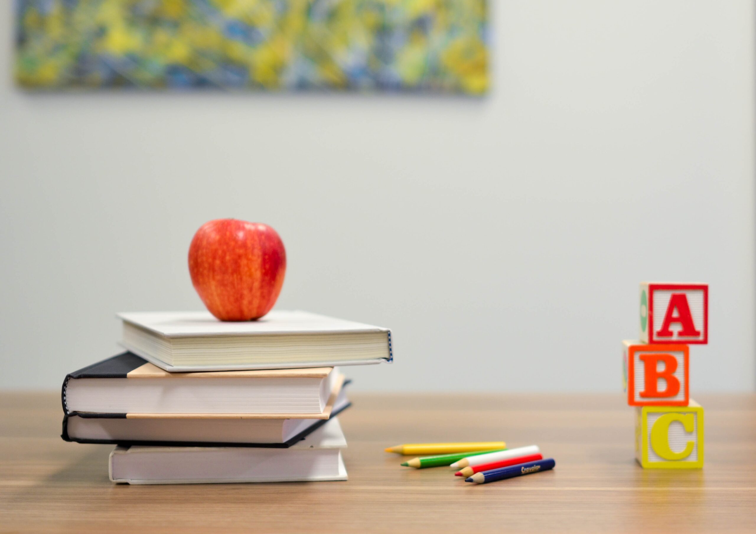 Teacher's desk at front of classroom, with books, blocks, crayons and a red apple.