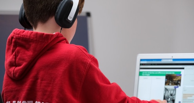 Bild eines Schülers, der Kopfhörer trägt und an einem Notebook arbeitet. Fähigkeiten für die Schulinformatik.